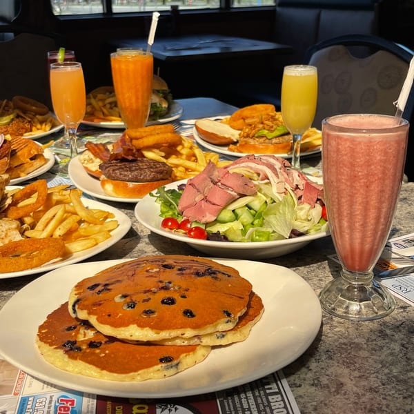 A diner table laden with blueberry pancakes, burgers, fries, onion rings, salad, and colorful drinks.