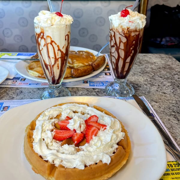 Candlelight Diner breakfast with a waffle, two milkshakes, pancakes, and sausage on a table.