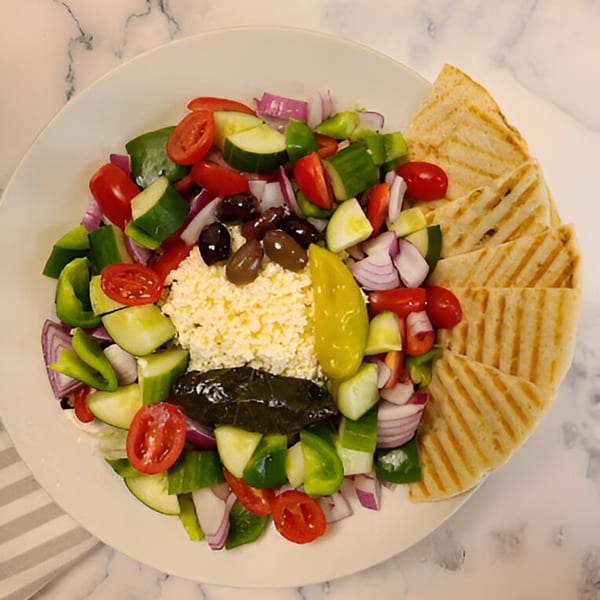 A vibrant Greek salad with feta, olives, and pita bread on a white plate at Candlelight Diner.