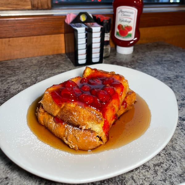 Candlelight Diner's French toast with cherry topping, powdered sugar, and maple syrup on a white plate.