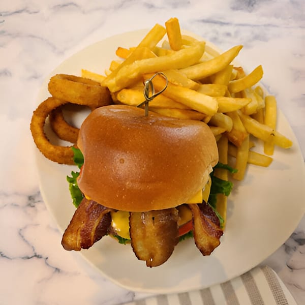 A bacon cheeseburger with fries and onion rings on a white plate at Candlelight Diner.