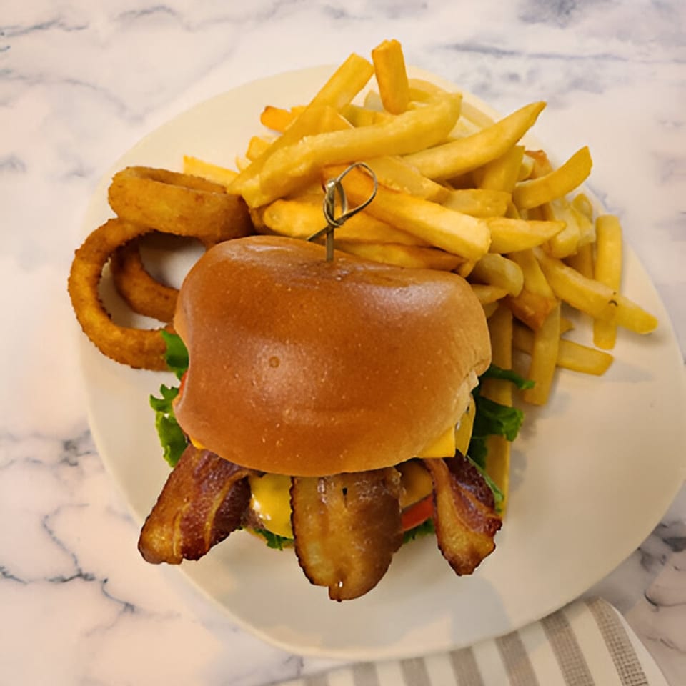 A bacon cheeseburger with fries and onion rings on a white plate at Candlelight Diner.