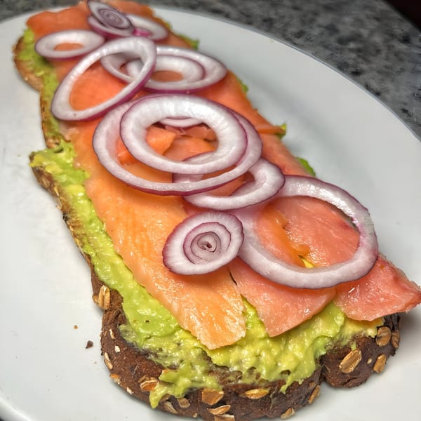 Avocado toast with smoked salmon and red onion rings on a white plate at Candlelight Diner.