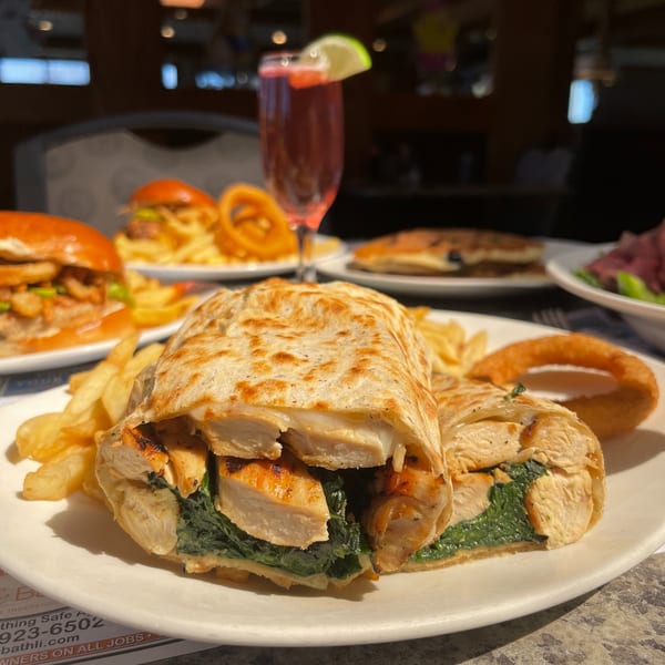 Chicken and spinach wrap with fries and an onion ring, with other diner food in the background.